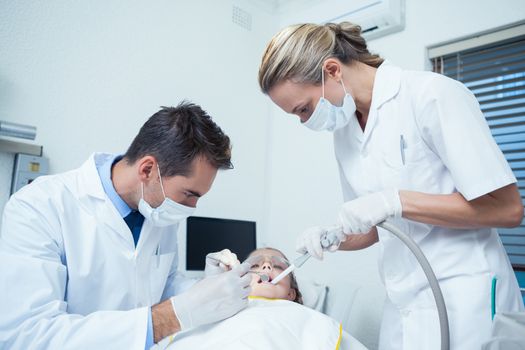 Male dentist  with assistant examining girls teeth in the dentists chair