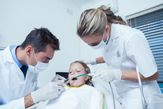 Male dentist  with assistant examining girls teeth in the dentists chair