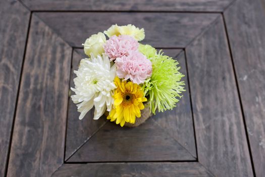a small bouquet of colorful flowers on a well used old desk or wooden surface.