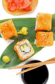 Maki Sushi with Salmon, Crab, Avocado and Cheese on Green Palm Leafs with Soy Sauce, Ginger and Pair of Chopsticks isolated on white background. Top View