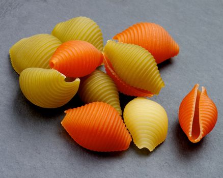 Stack of Raw Conchiglie Tricolore Pasta with Inscription closeup on Black Stone background