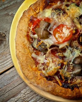 Homemade Pizza with Forest Mushrooms, Tomatoes and Grated Cheese Cross Section on Circle Cutting Board on Wooden background. Top View