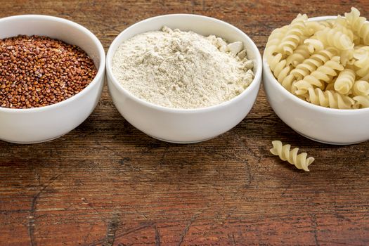 gluten free quinoa grain, flour and pasta - three small ceramic bowls against rustic wood with a copy space