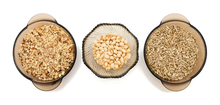 Food ingredients: walnuts crushed, peeled sunflower seeds, nuts, peanuts in a glass on a white background, top view