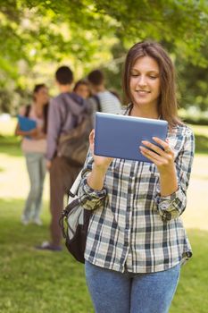 Smiling student with a shoulder bag and using tablet computer in park at school