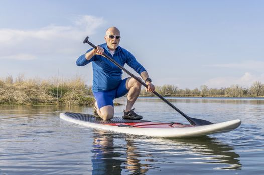 Senior male on stand up paddling (SUP) board. Early spring on calm lake in Colorado.