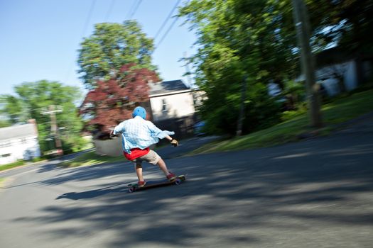 Longboarder skating on an urban road. Slight motion blur from panning technique to capture movement.