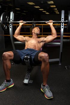 Weight lifter at the bench press lifting a barbell on an incline bench.