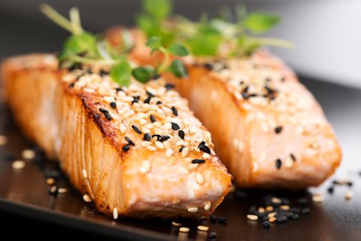 Grilled salmon, sesame seeds  and marjoram on a black plate. Studio shot