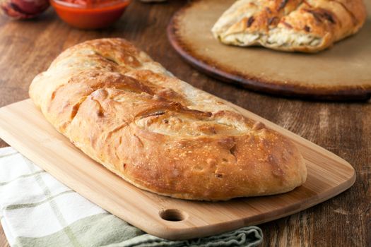 Homemade stromboli or stuffed bread with broccoli potatoes garlic onions and mozzarella cheese along with a side of marinara dipping sauce.