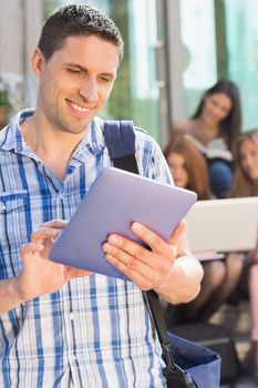 Happy student using his tablet pc on campus at the university