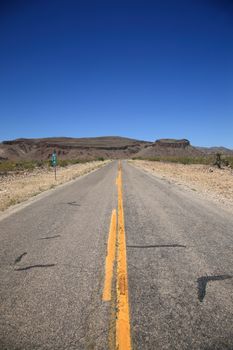 Desert road heads towards the mountains and buttes in Southwestern United States