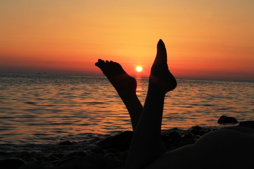 Naked woman legs and evening beach on the sunset