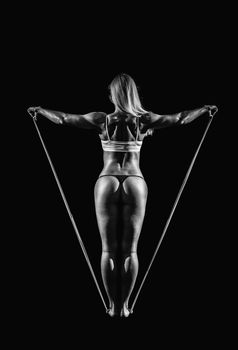 Sportswoman exercising with a resistance band on black background.