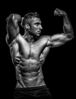 Handsome muscular bodybuilder posing over black background