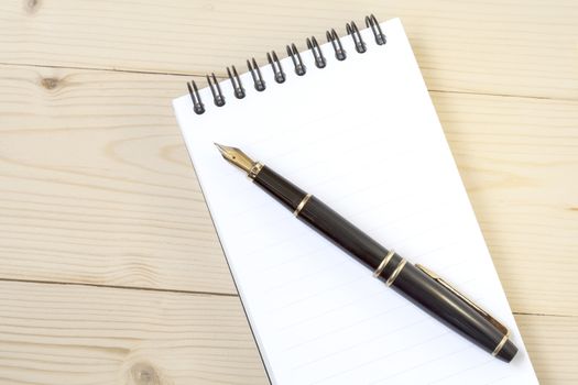 blank notebook with elegant golden fountain pen on wooden 
background.