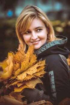 woman with autumn leaves in hand and fall yellow maple garden background