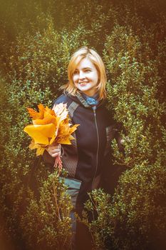 woman with autumn leaves in hand and fall yellow maple garden background