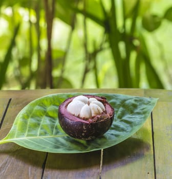 Single Mangostin and Fresh Green Leaf on Wooden Table