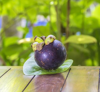 Single Mangostin and Fresh Green Leaf on Wooden Table