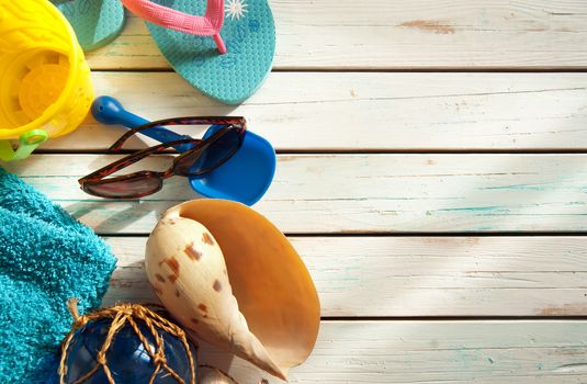 Beach items including towel, sunglasses and bucket and spade over wood panels