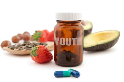 Anti-aging pills surrounded by nutritious superfoods including avocado, pumpkin seeds and berries