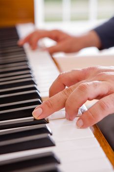 Man playing the piano with a close up view of his hands on the open keyboard as he stretches for a note