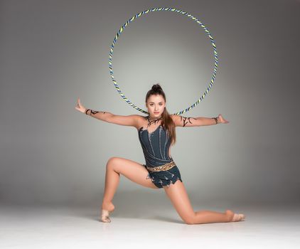teenager doing gymnastics exercises with colorful hoop on a gray background