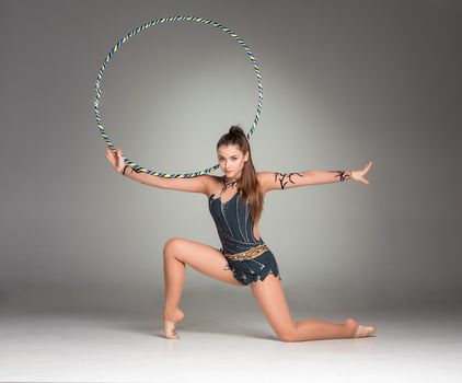 teenager doing gymnastics exercises with colorful hoop on a gray background