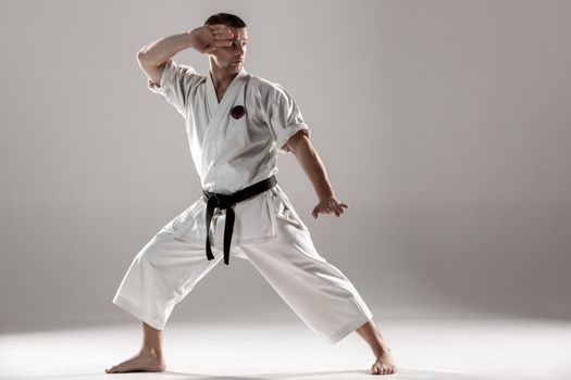 Man in white kimono and black belt training karate over gray background.