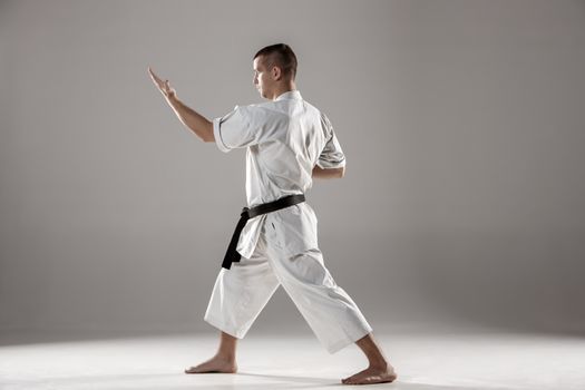 Man in white kimono and black belt training karate over gray background.