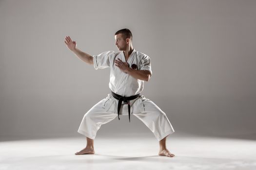 Man in white kimono and black belt training karate over gray background.