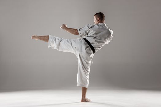 Man in white kimono and black belt training karate over gray background.