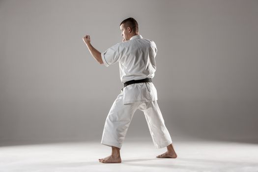 Man in white kimono and black belt training karate over gray background.