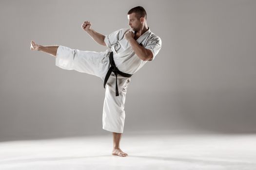 Man in white kimono and black belt training karate over gray background.