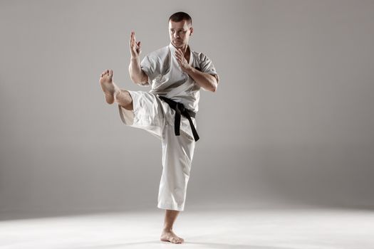 Man in white kimono and black belt training karate over gray background.