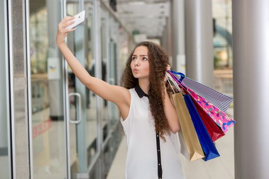 beautiful young woman goes shopping using a smartphone with a shopping bags in the mall