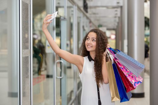 beautiful young woman goes shopping using a smartphone with a shopping bags in the mall