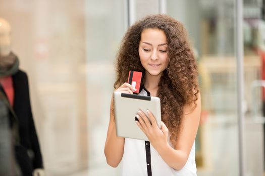 Beautiful young girl paying by credit card for shopping with a laptop against the background of the shopping center