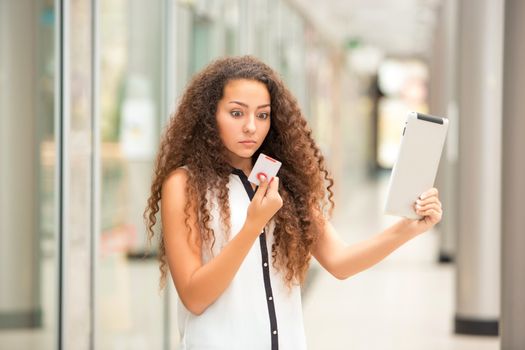 Beautiful young girl paying by credit card for shopping with a laptop against the background of the shopping center