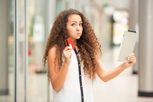 Beautiful young girl paying by credit card for shopping with a laptop against the background of the shopping center