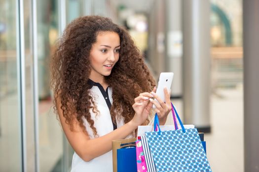 beautiful young woman goes shopping using a smartphone with a fashion store window with manikin in the background.