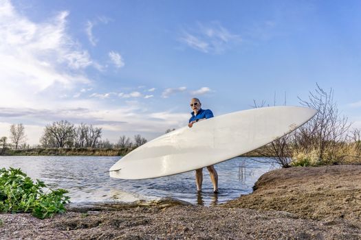 senior male paddler is launching his paddleboard on a lake, early spring in Colorado