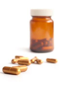 Golden capsules with medical jar over a white background