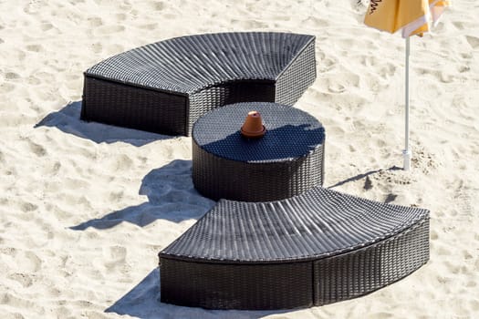 Modern dark brown outdoor rounded furniture with table and umbrella on sunlit beach