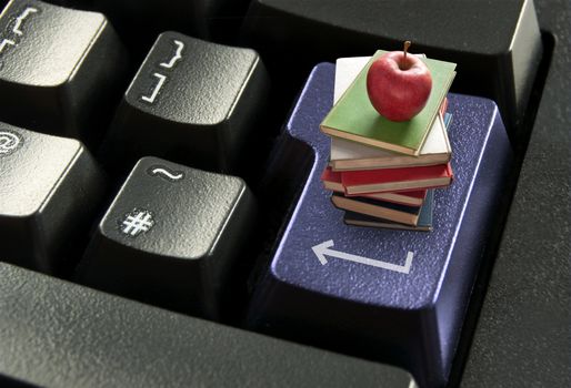 Stack of books with red apple on top of a computer enter key