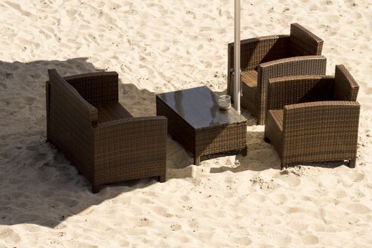 Brown outdoor sofa chairs and table on white sand beach