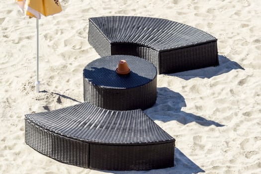 Modern dark brown outdoor rounded furniture with table and umbrella on sunlit beach