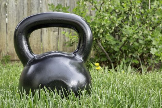 heavy iron black kettlebell on green grass in backyard - outdoor fitness concept