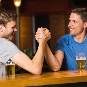 Happy friend arm wrestling each other in a bar